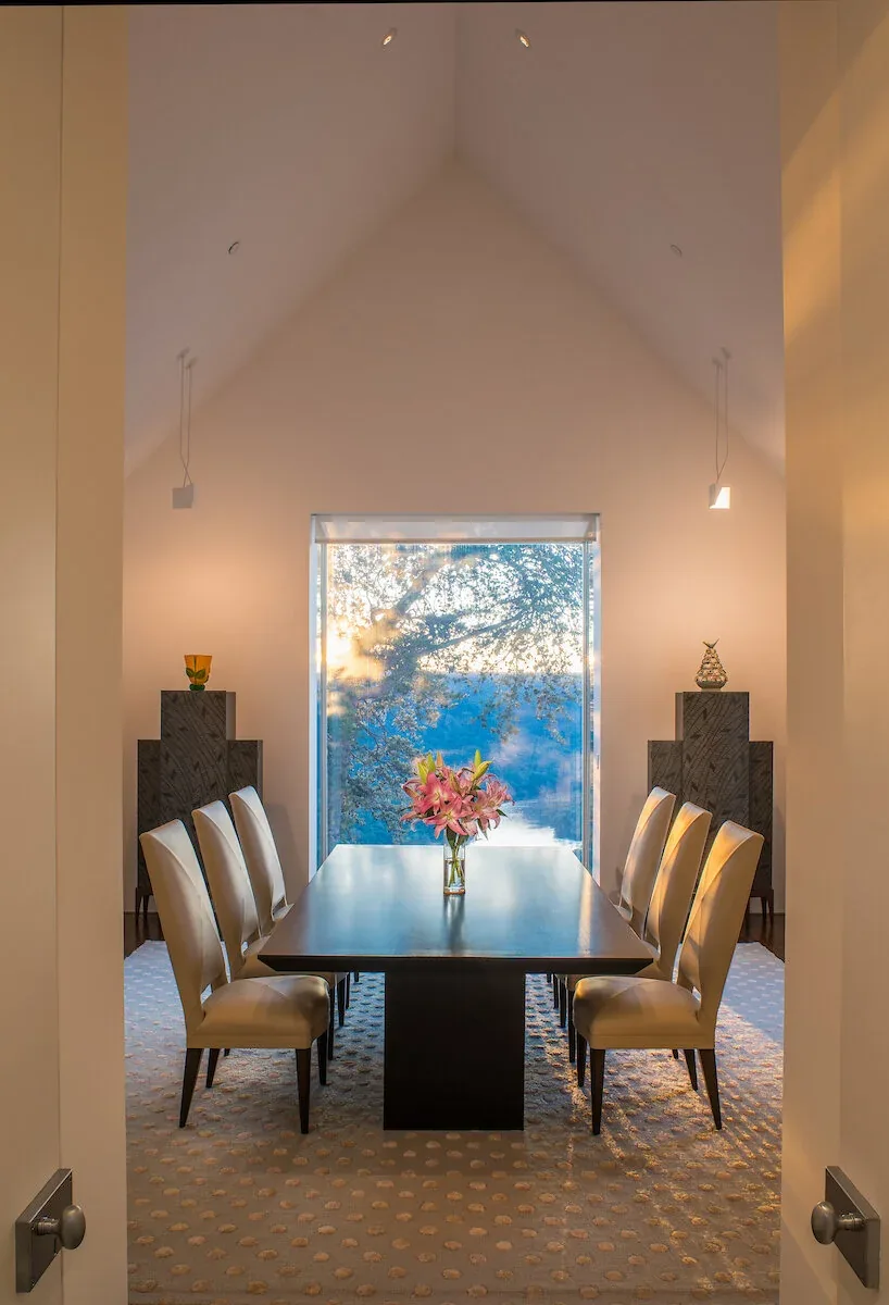 The Mills Residence dining area by Jacobsen Architecture features a symmetrical arrangement facing a large window with river views.