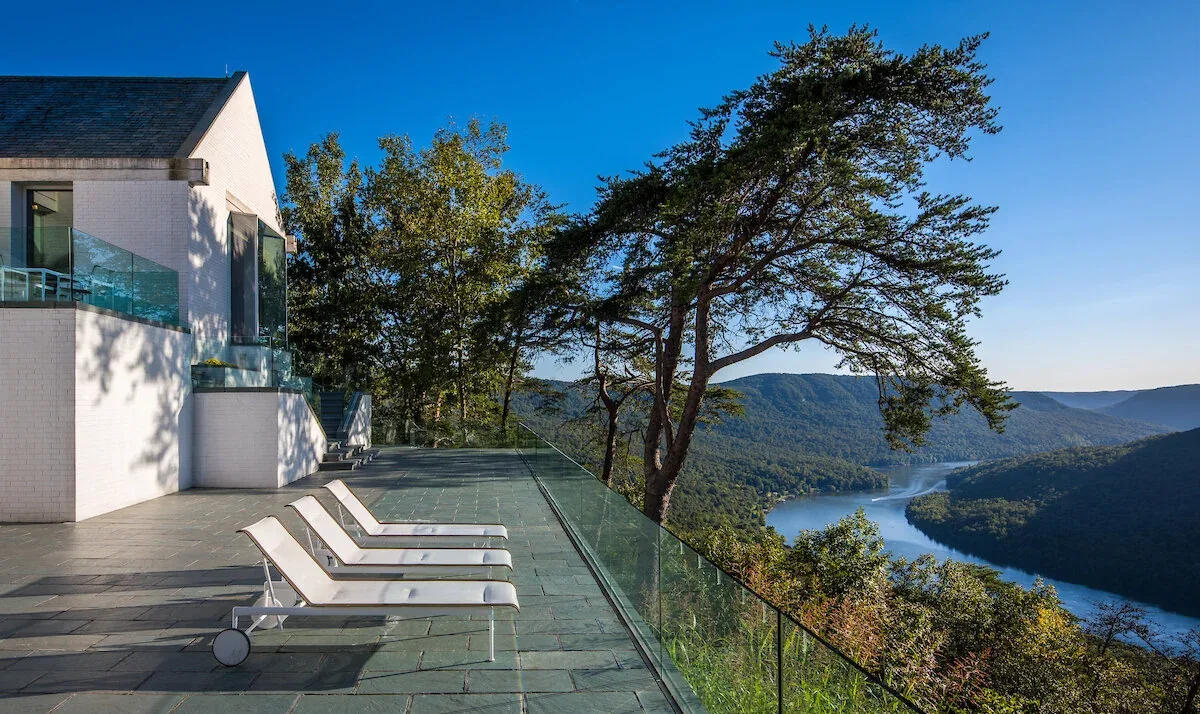 The Mills Residence features a terrace with stone flooring, glass railing, and a river view in the distance.