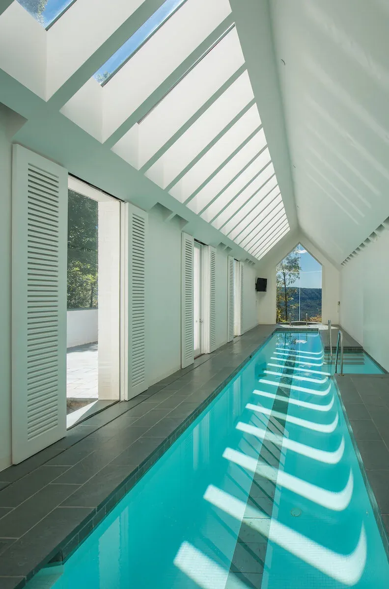 The Mills Residence features an indoor plunge pool with a vaulted ceiling and skylights, overlooking a scenic river view.