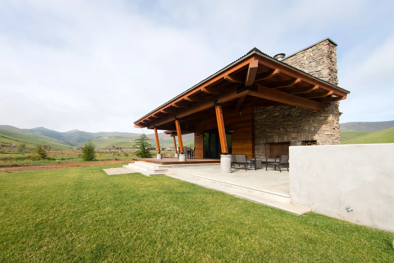 The Cayucos Ranch patio features angled wood beams, a corrugated metal roof, and a prominent stone fireplace.