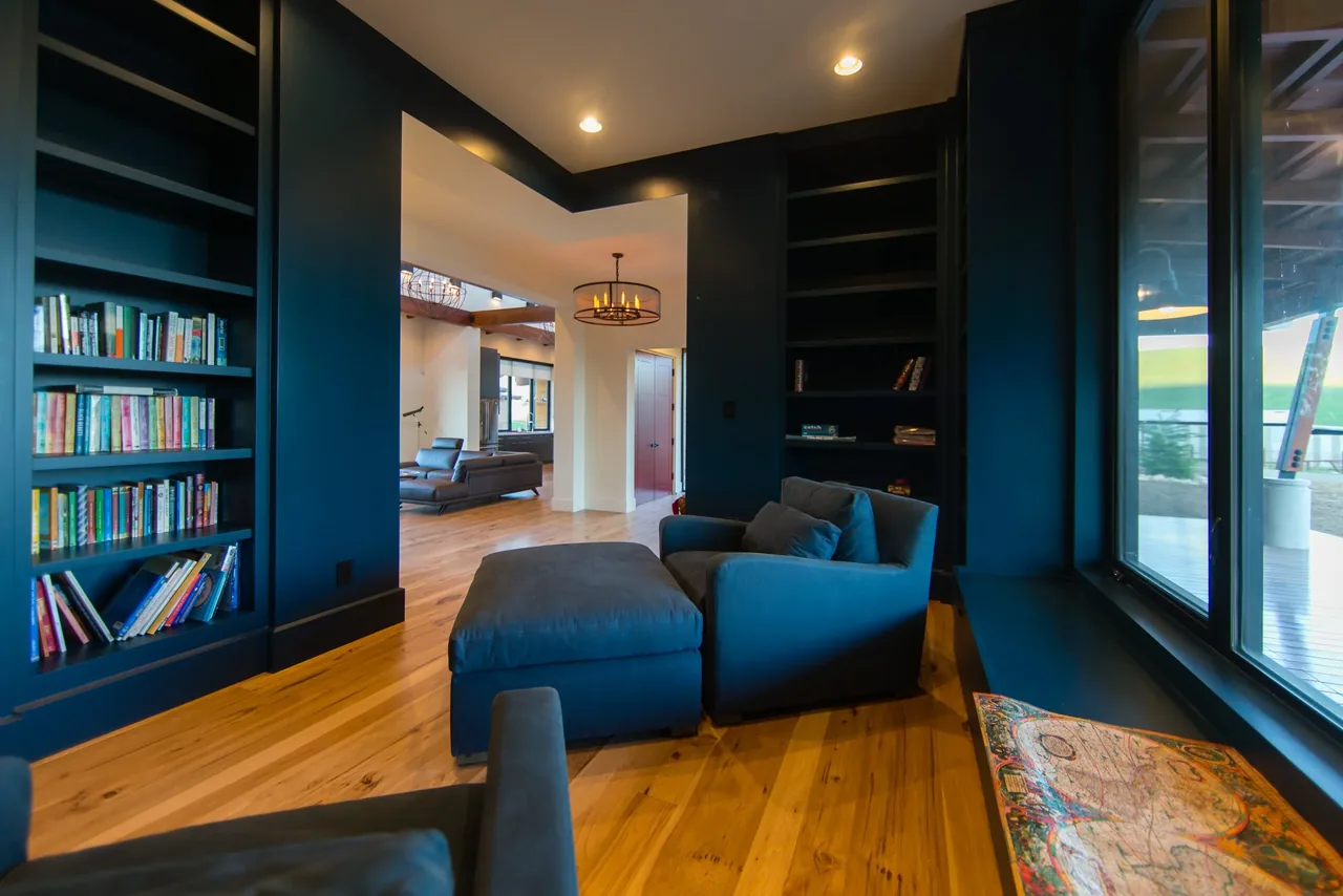 Living area features dark built-in bookshelves, wood flooring, and large windows to outdoor patio in the Cayucos Ranch project.