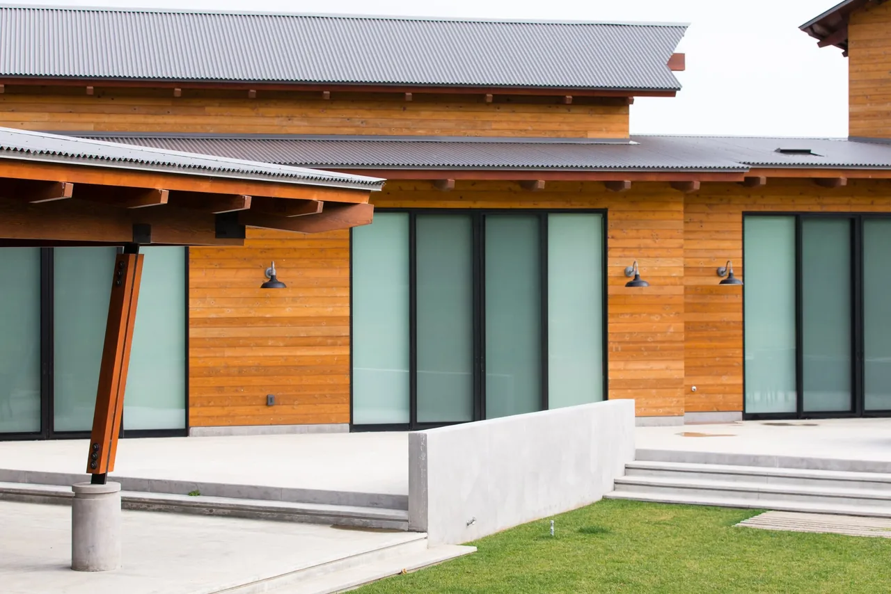 Cayucos Ranch features wood siding and frosted glass sliding doors under a metal shed roof with angled wooden beams.