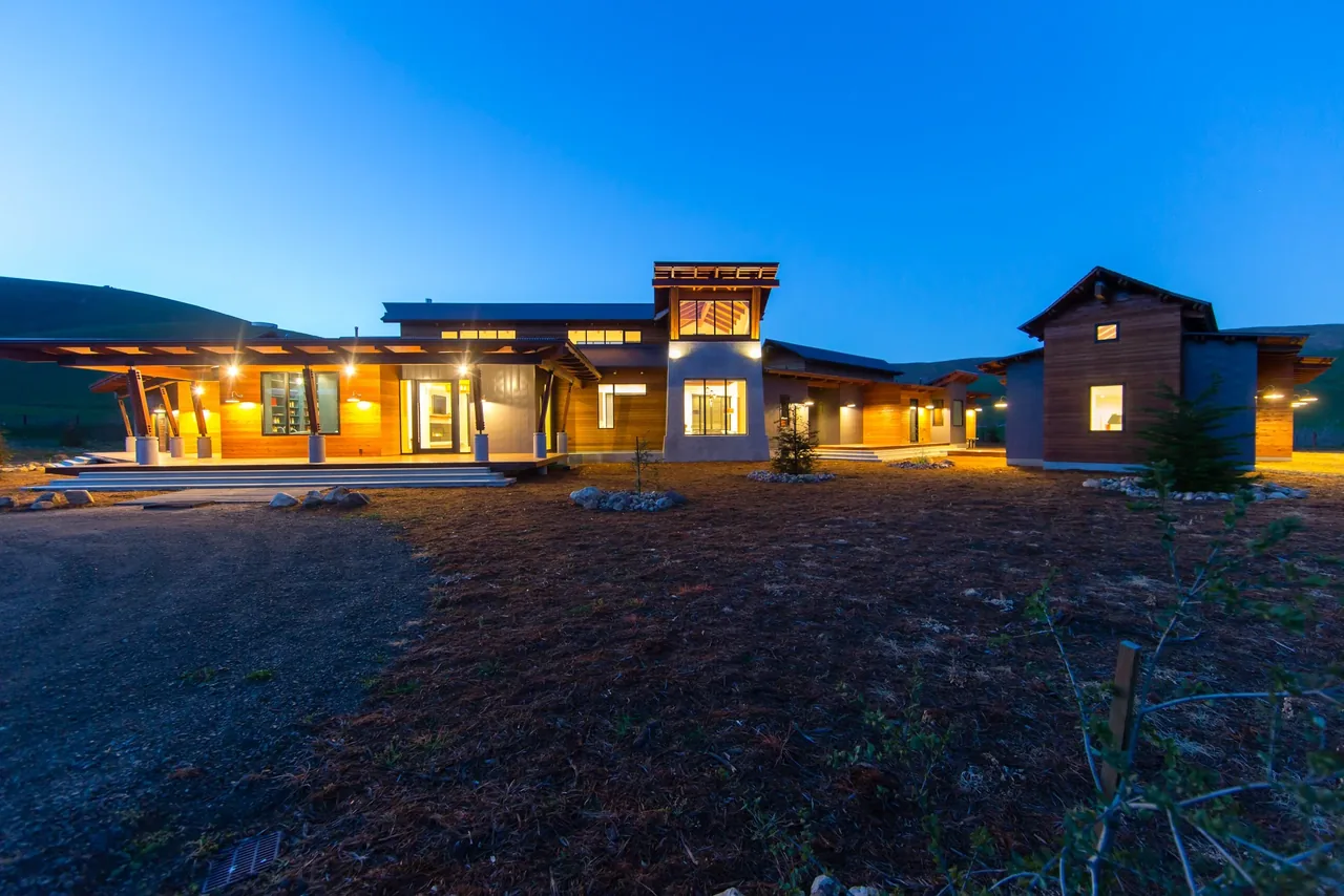 Modern ranch house exterior with wood siding and illuminated windows at dusk in Cayucos Ranch project.
