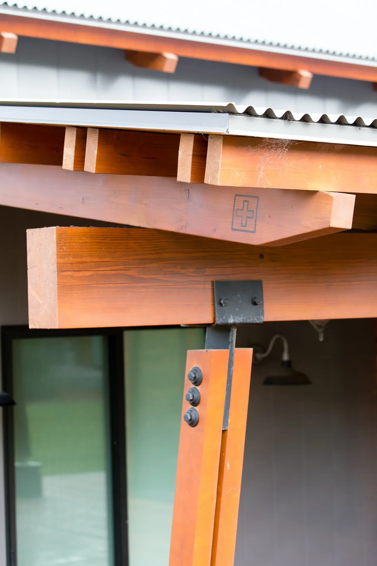 Angled wood beams with metal connectors supporting a corrugated metal roof section.