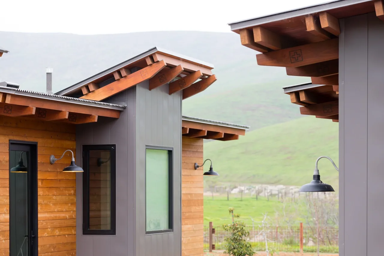 Cayucos Ranch features wood siding, gray metal siding, angled beams, and outdoor lighting with a multi-structure layout.