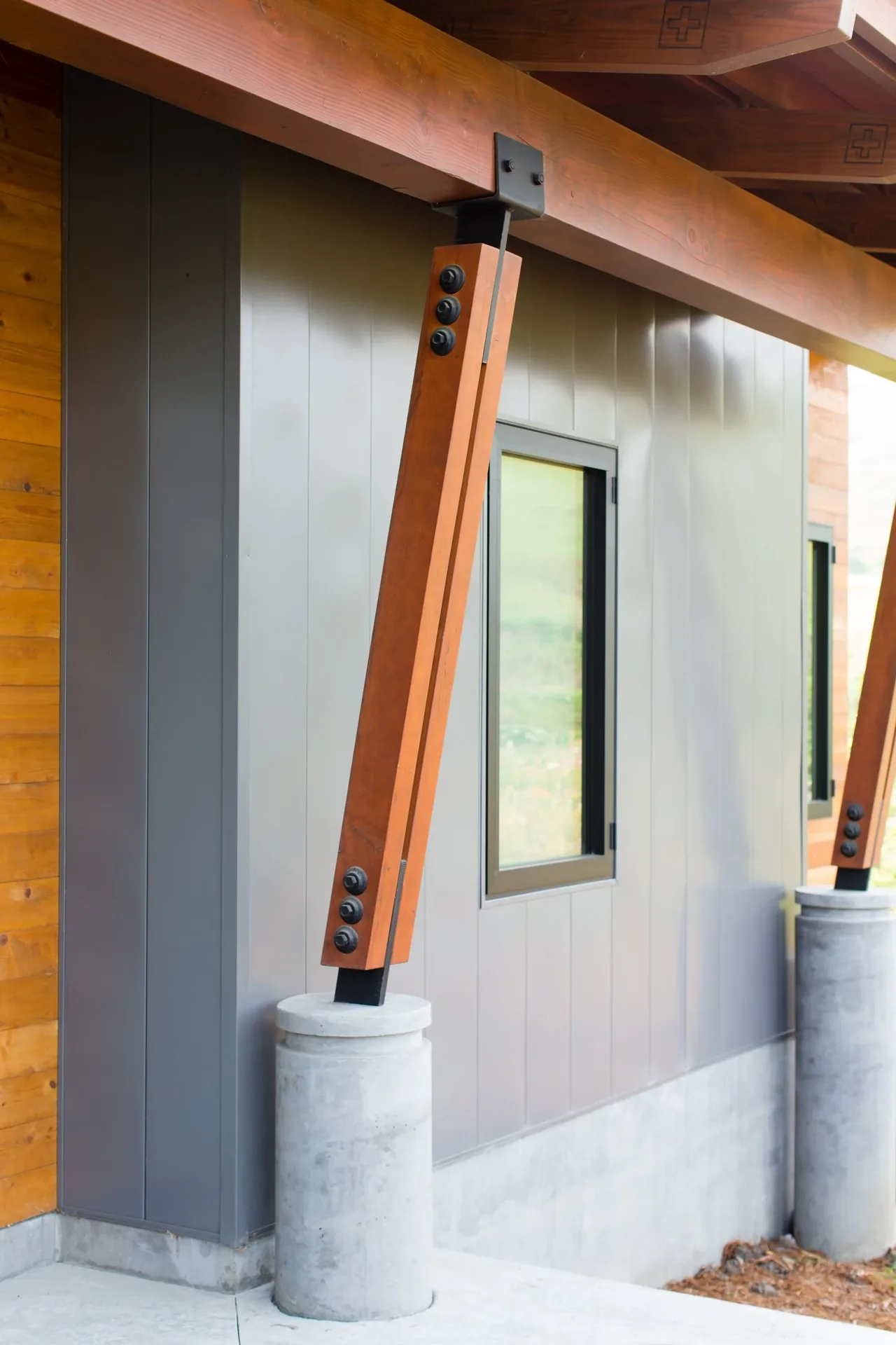 Modern exterior wall features angled wood support beams on concrete bases with sleek gray siding.