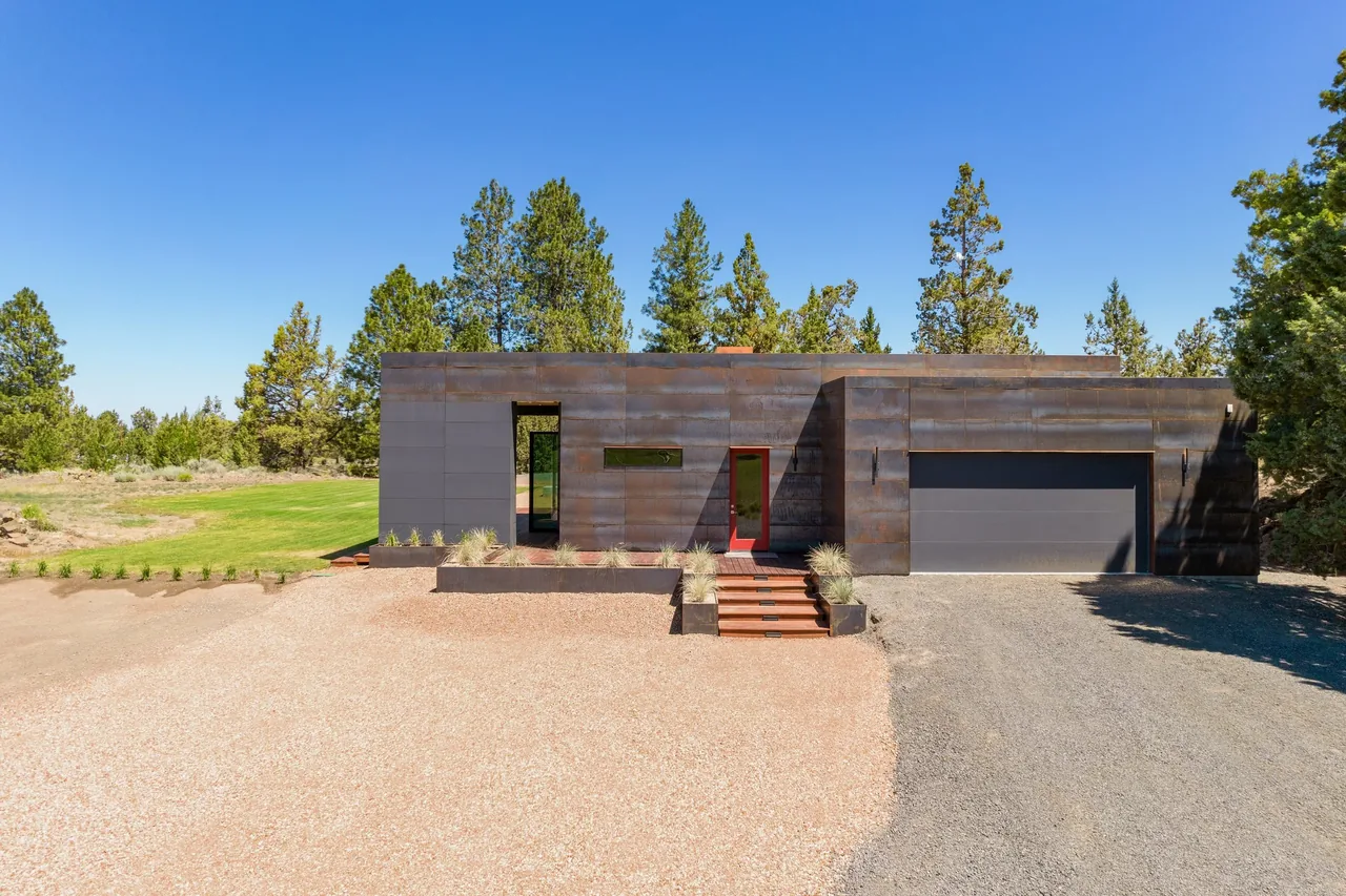 The Schibel Road Residence by Crabtree Architecture + Design features a flat roof and blackened steel facade with large garage and minimal landscaping.