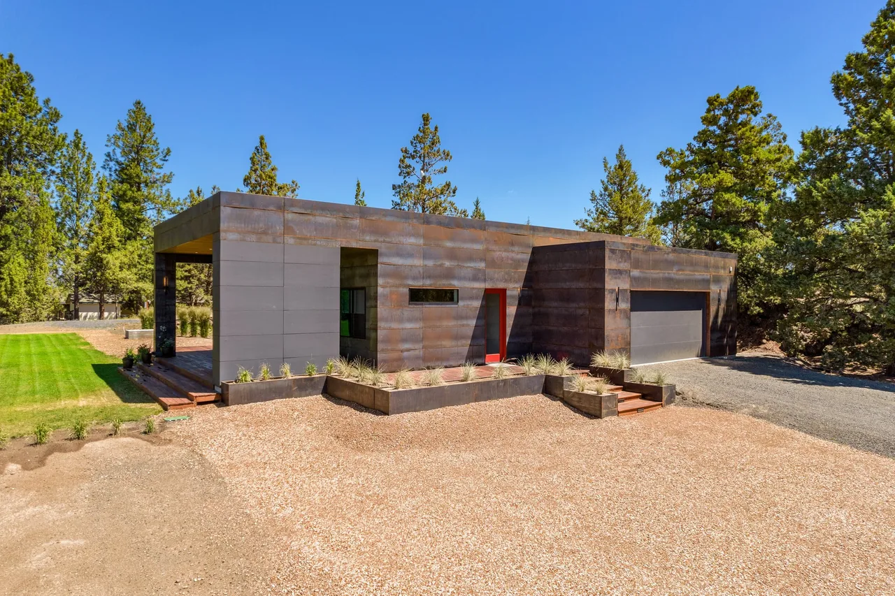 The Schibel Road Residence features a rust-colored metal exterior with a bright red entry door and rectangular windows.