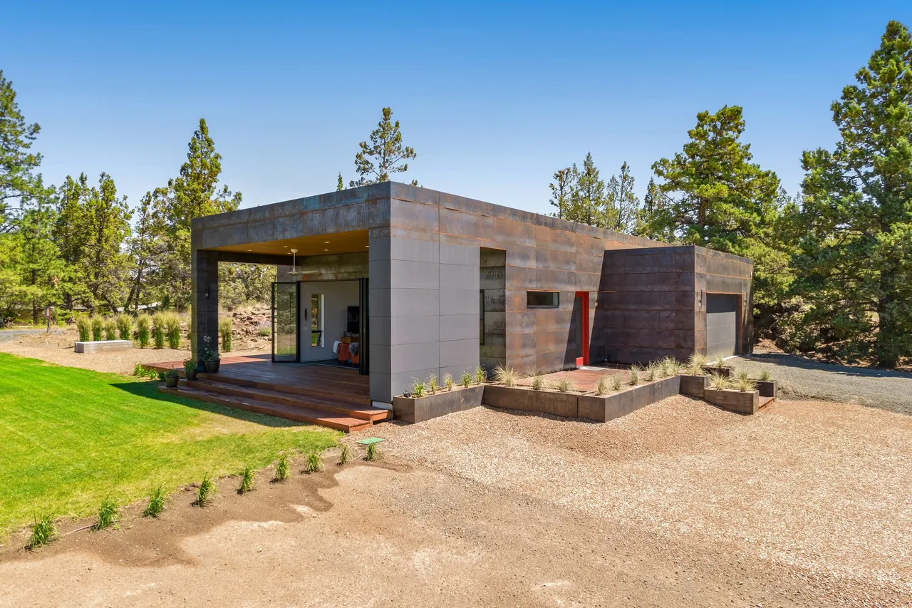 Schibel Road Residence by Crabtree Architecture + Design features a rust-colored metal exterior with flat roof and red entry door.