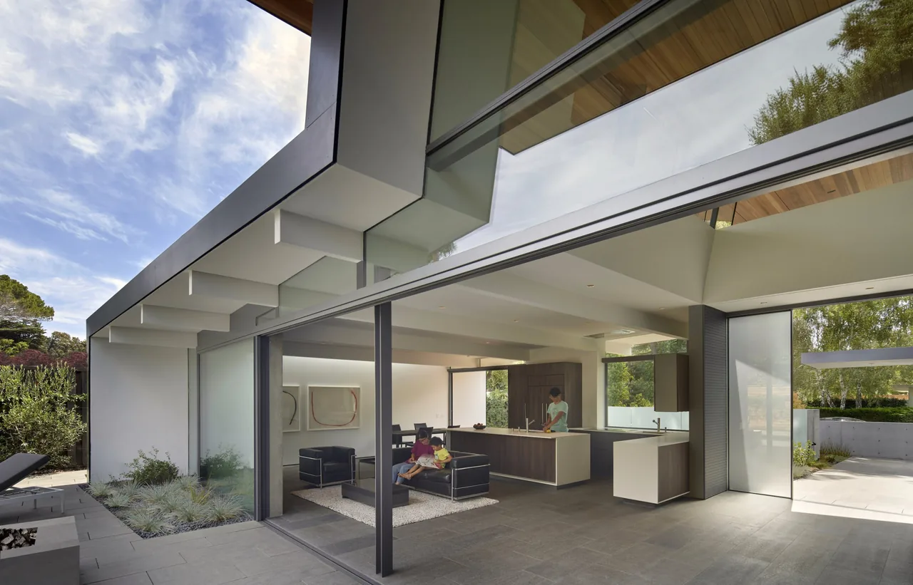Edgewood House features large sliding glass doors connecting the interior living and kitchen spaces to the outdoor patio under a wood soffit ceiling.