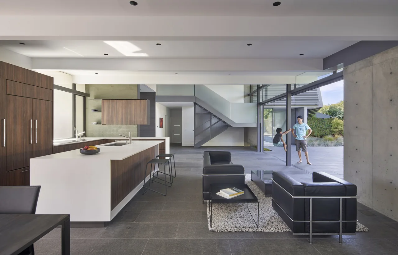 Edgewood House interior by Terry & Terry Architecture features an open-plan kitchen and living space with stone flooring and glass walls.
