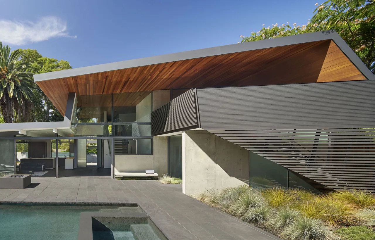 Edgewood House features a dark gray exterior with wood soffit ceiling and large glass windows alongside a pool.