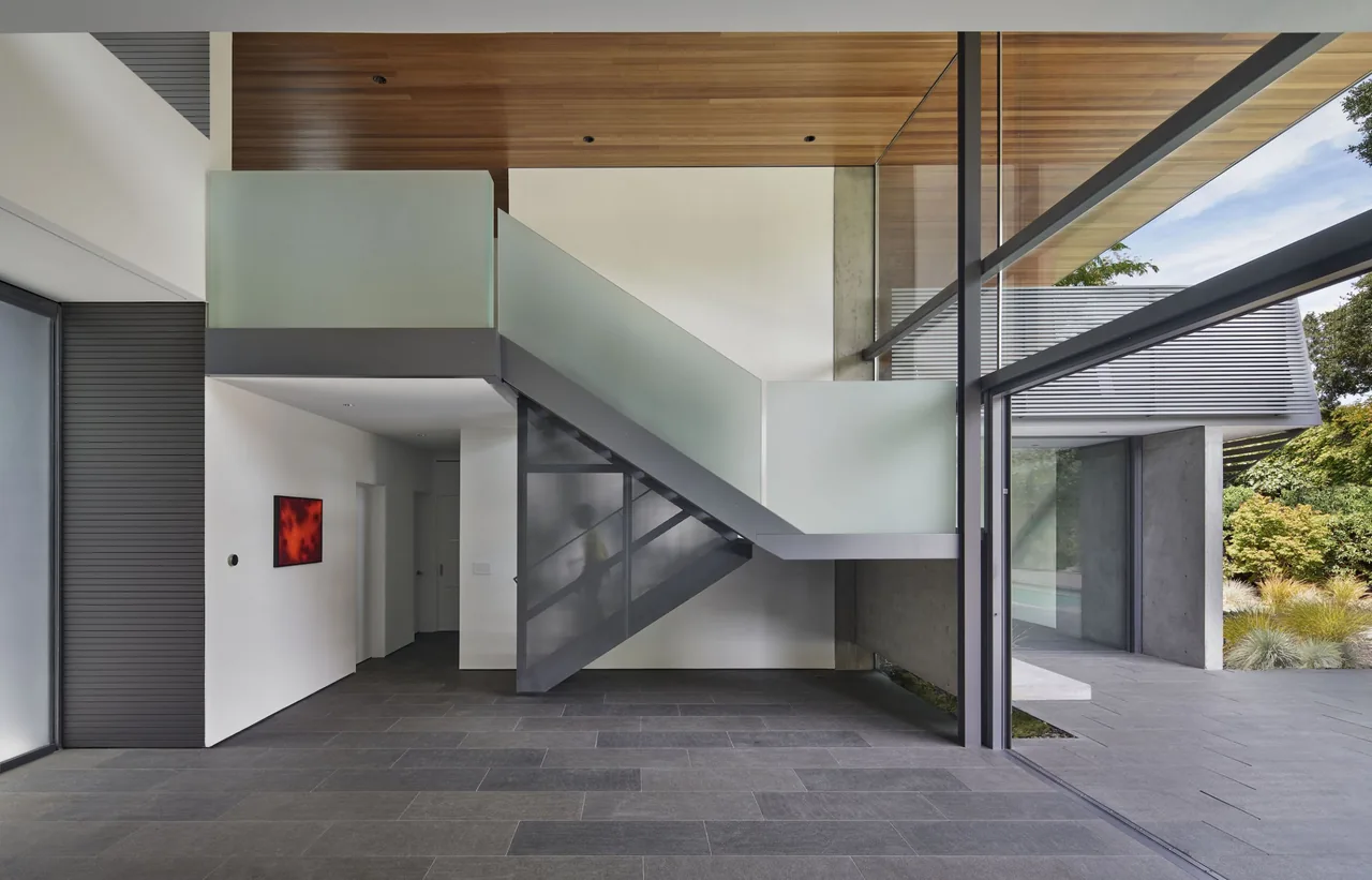 Edgewood House entry with a wood soffit ceiling, floating stairs with frosted glass panels, and large glass windows.