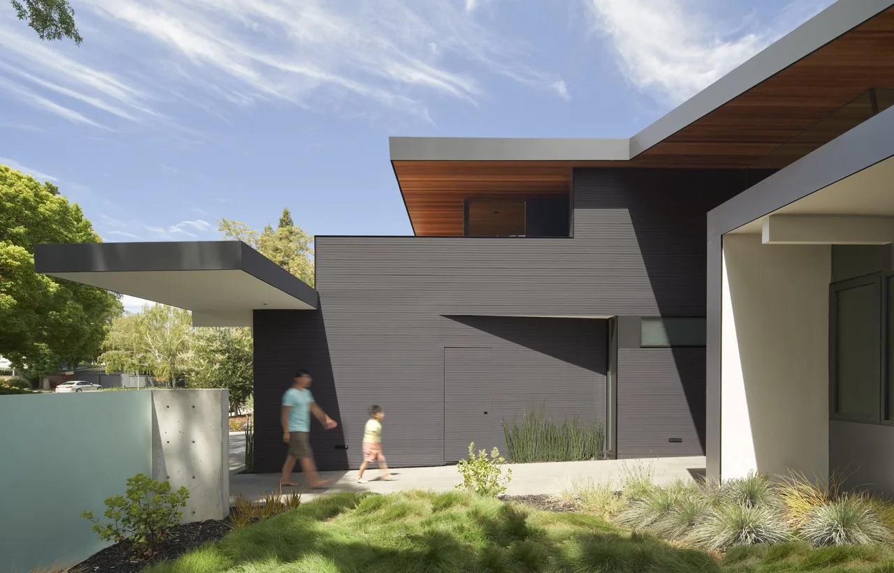 Edgewood House features a dark gray exterior with flat roofs and wood soffits, showcasing mature landscaping near the entrance.
