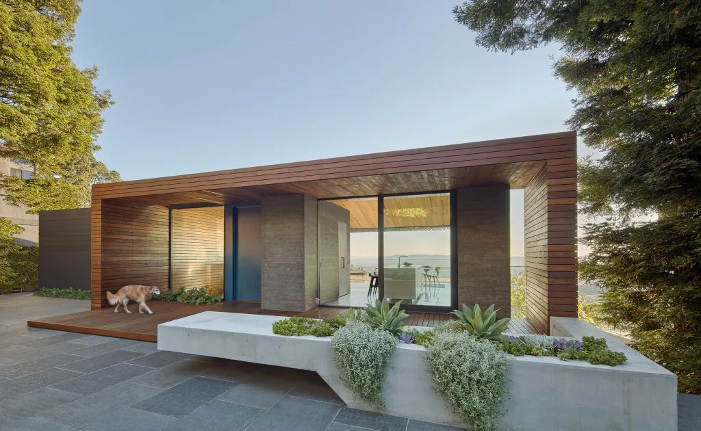 Skyline House features a modern design with wood siding and glass walls opening to a patio.