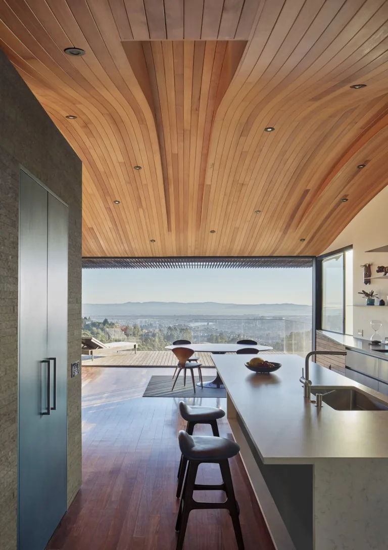 Skyline House kitchen with curved wood ceiling and extending to outdoor dining with expansive views.