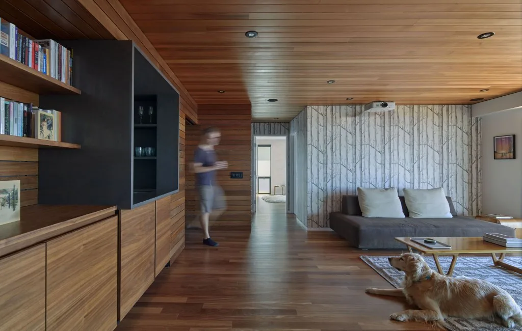 Living room featuring wood-paneled ceiling and walls, wallpaper with tree design, and a golden retriever on the rug.