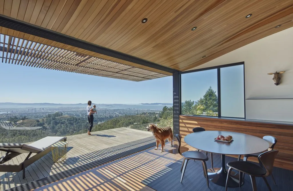 Skyline House dining area with wood-paneled ceiling opens to deck overlooking landscape and city views.