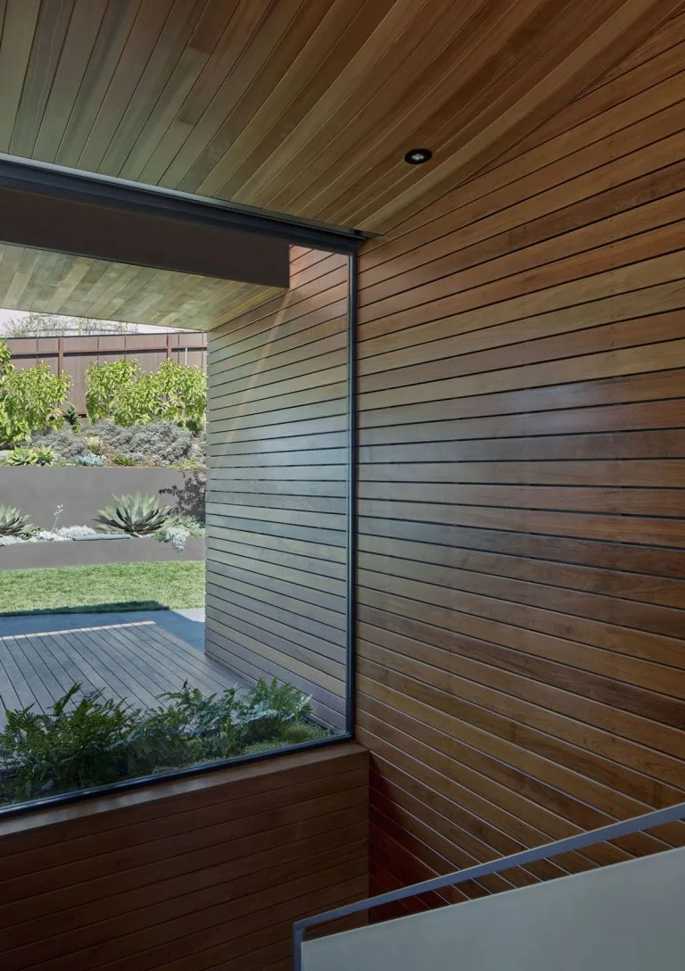 Horizontal wood paneling wraps a stairwell wall and ceiling with a large window framing the outdoor garden space.