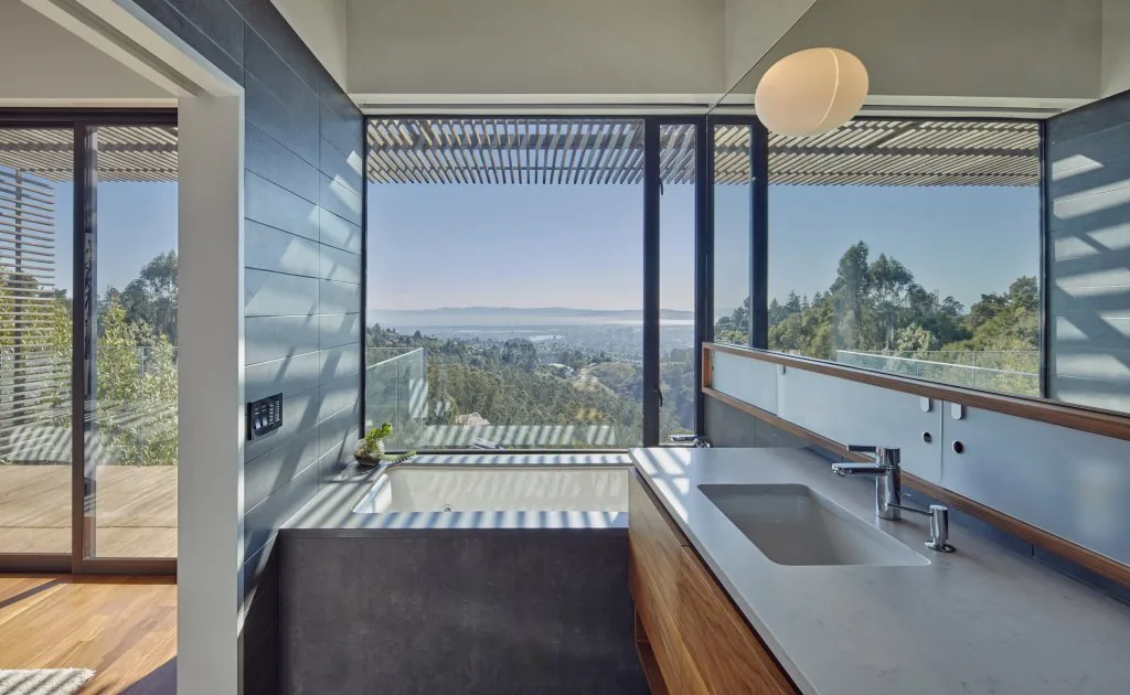 The Skyline House bathroom features floor-to-ceiling glazing with valley views and a modern wood vanity with an undermount sink.