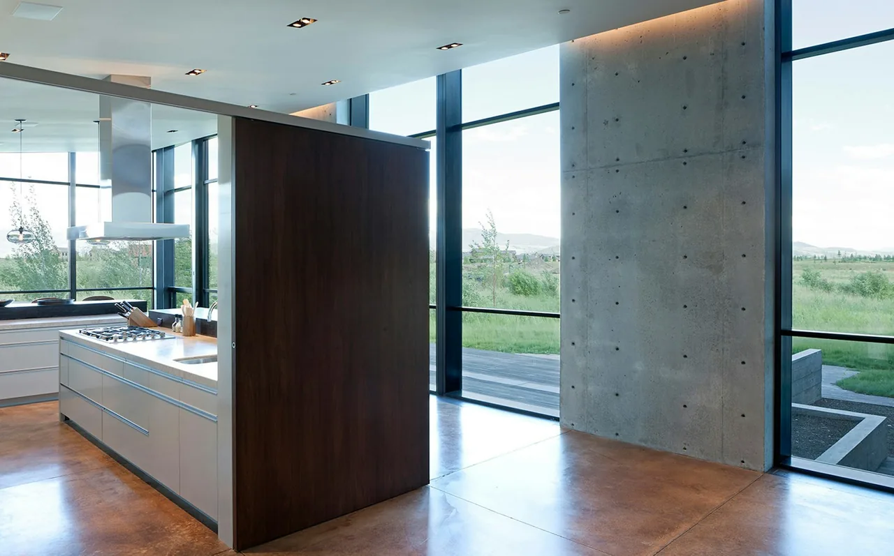 Diagonal House kitchen features concrete walls, floor-to-ceiling corner windows, and a central kitchen island by Stephen Dynia Architects.