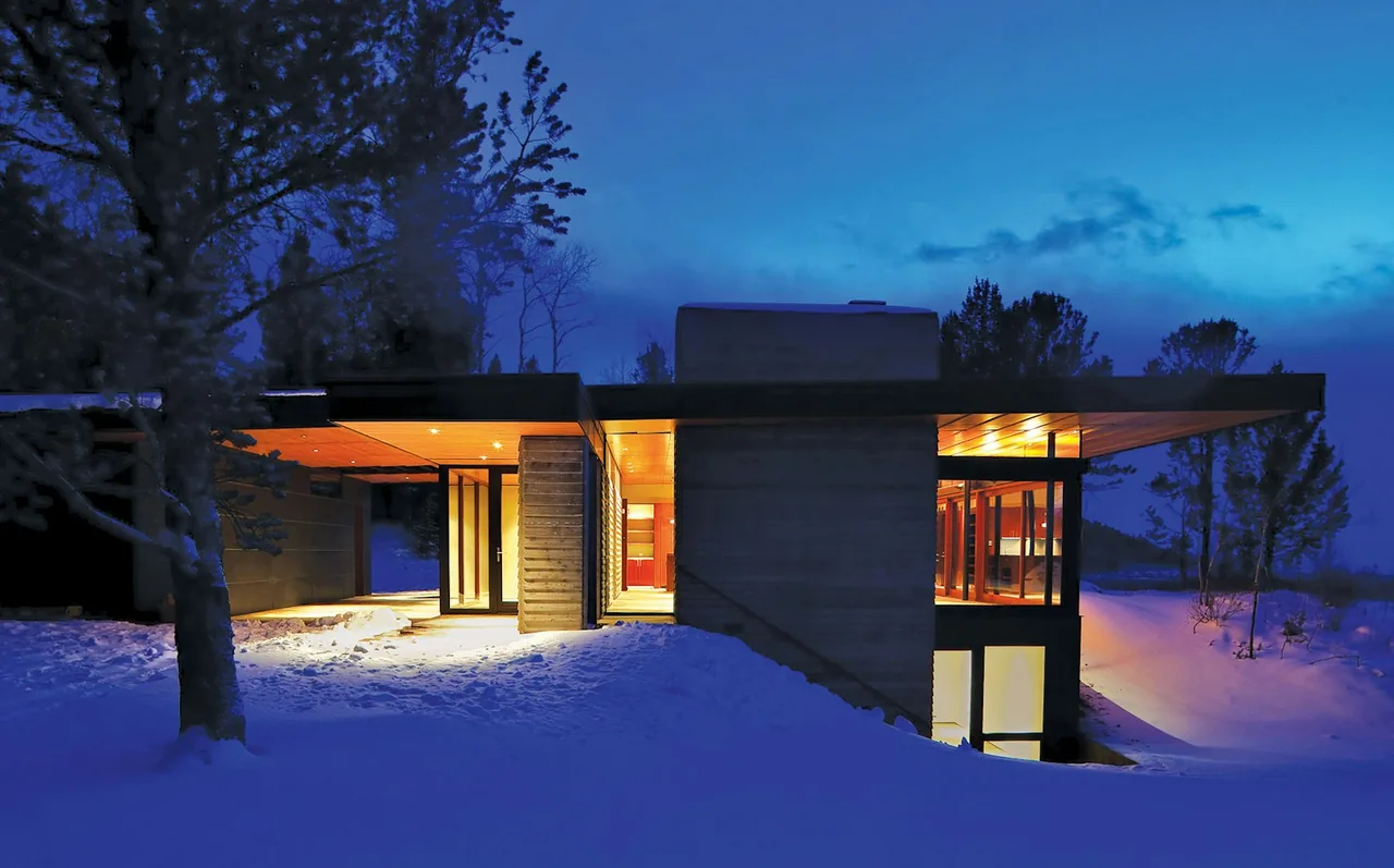 Lost Creek Cabin shows modern design with illuminated interiors and a large wood-paneled overhanging roof at night.