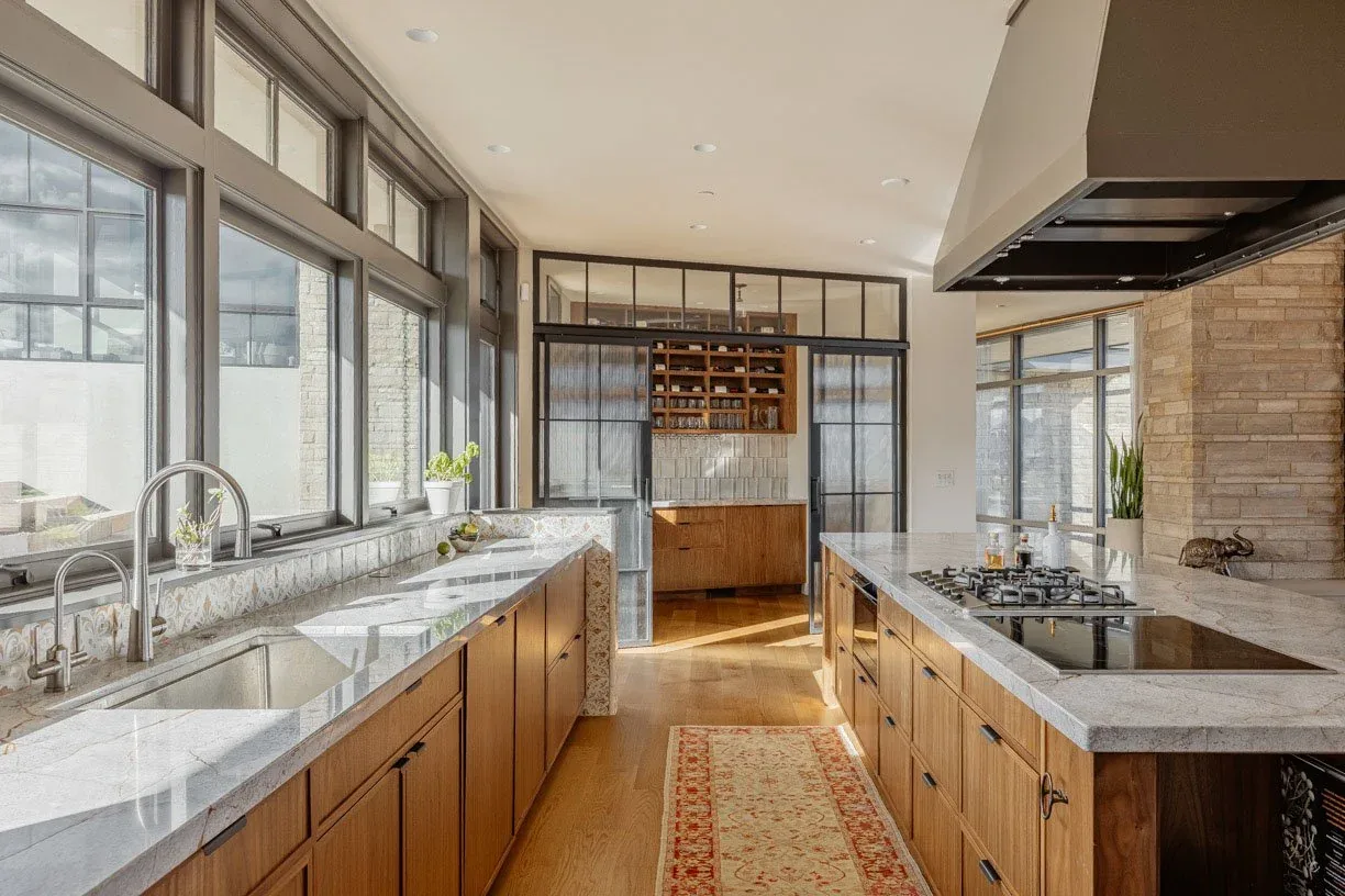 Kitchen of Boulder Mountain Residence features wood cabinetry, stone counters, black-framed windows, and a large hood over the island cooktop.