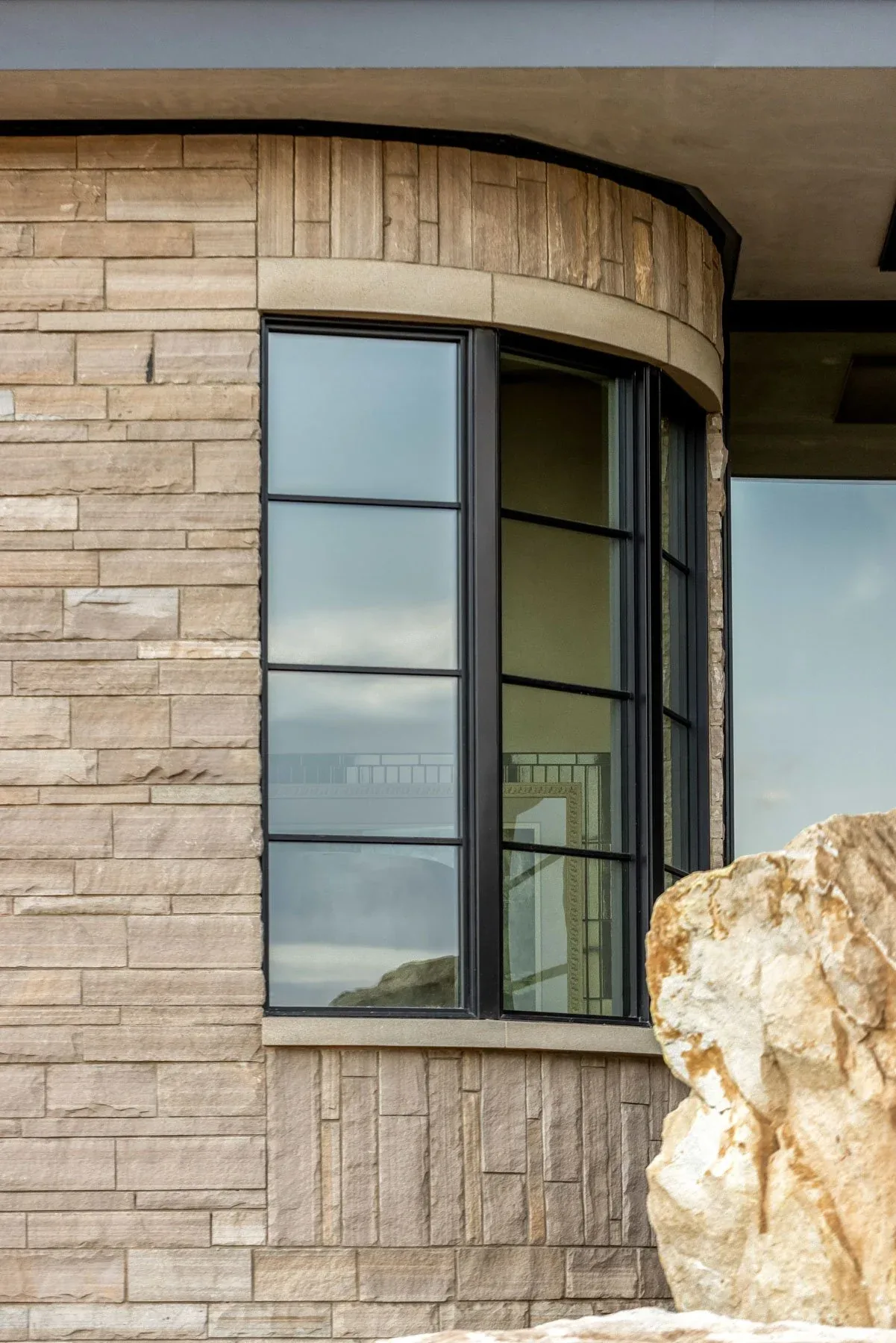 Curved stone exterior wall with black metal-framed windows at Boulder Mountain Residence by skB Architects.