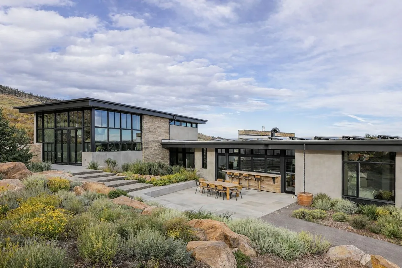 Modern Boulder Mountain Residence features large black-framed windows and stone landscaping on a hillside.