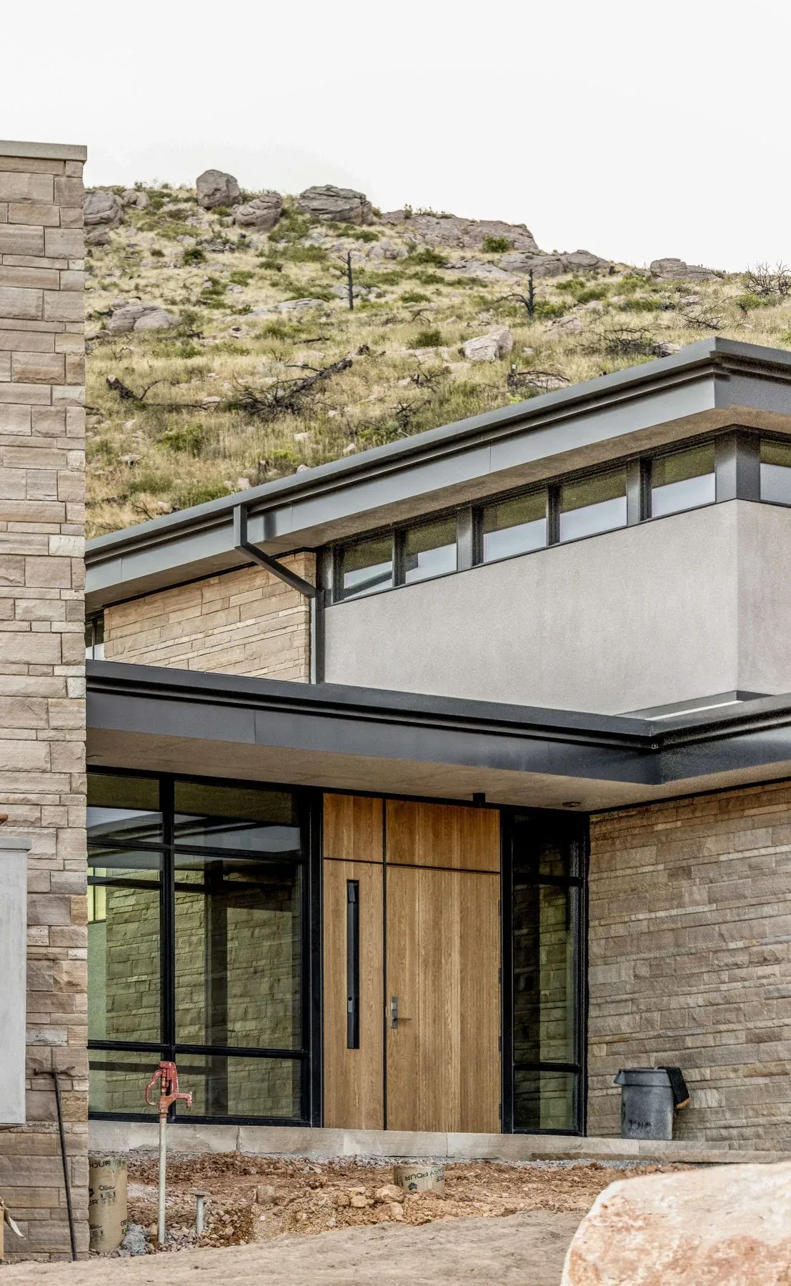 Entry of Boulder Mountain Residence features a wooden front door and stone siding with black window frames under a flat roof.
