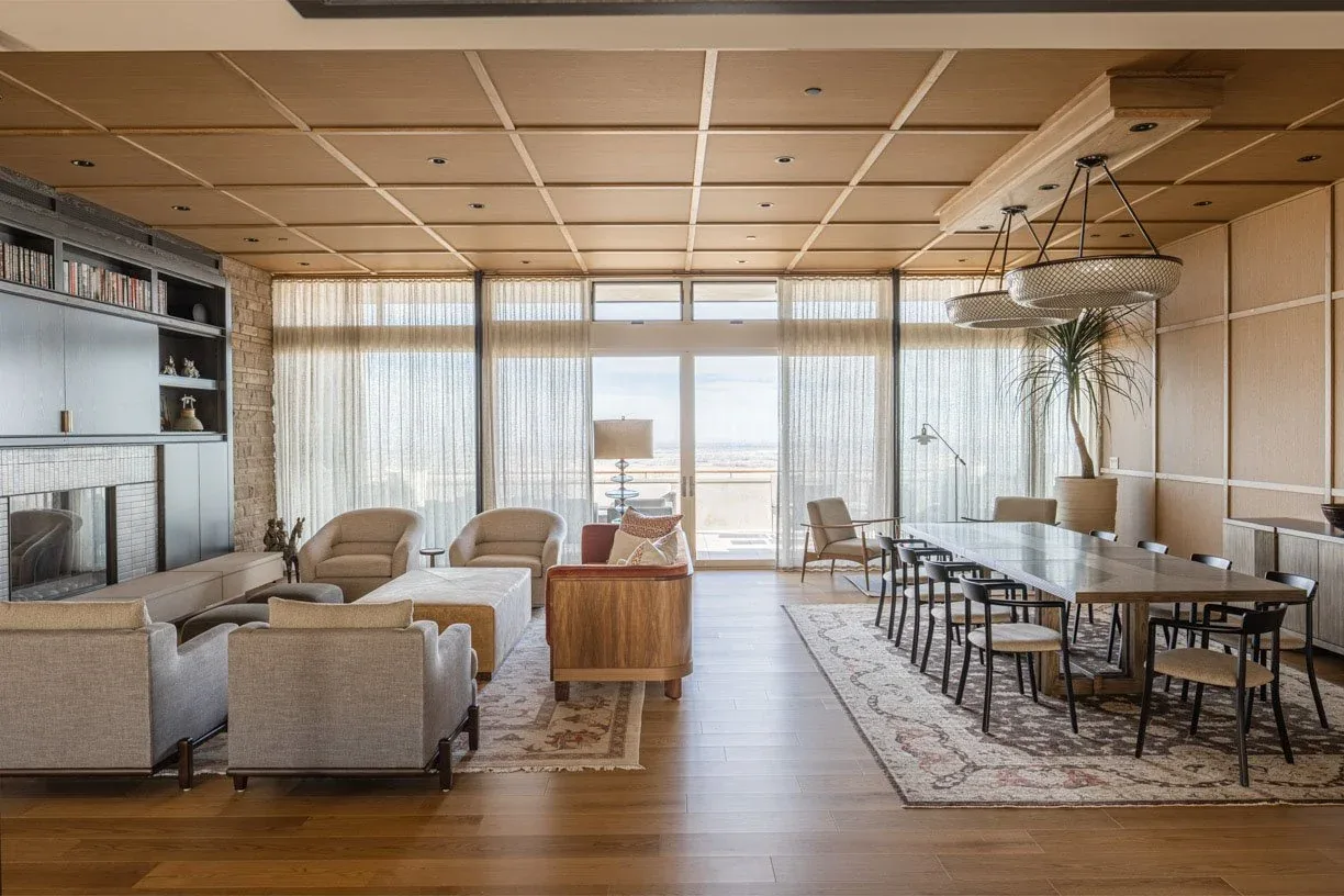 Living and dining area with wood panel ceiling, floor-to-ceiling windows, and a large dining table with black chairs.
