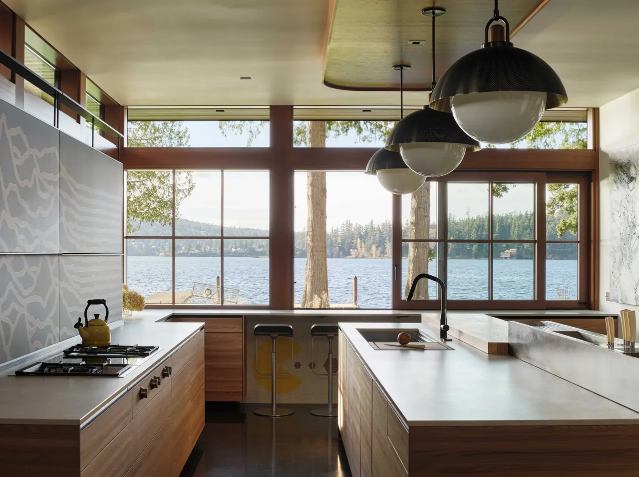 Kitchen with expansive corner windows offering a lake view, featuring wood grain cabinets and pendant lighting.
