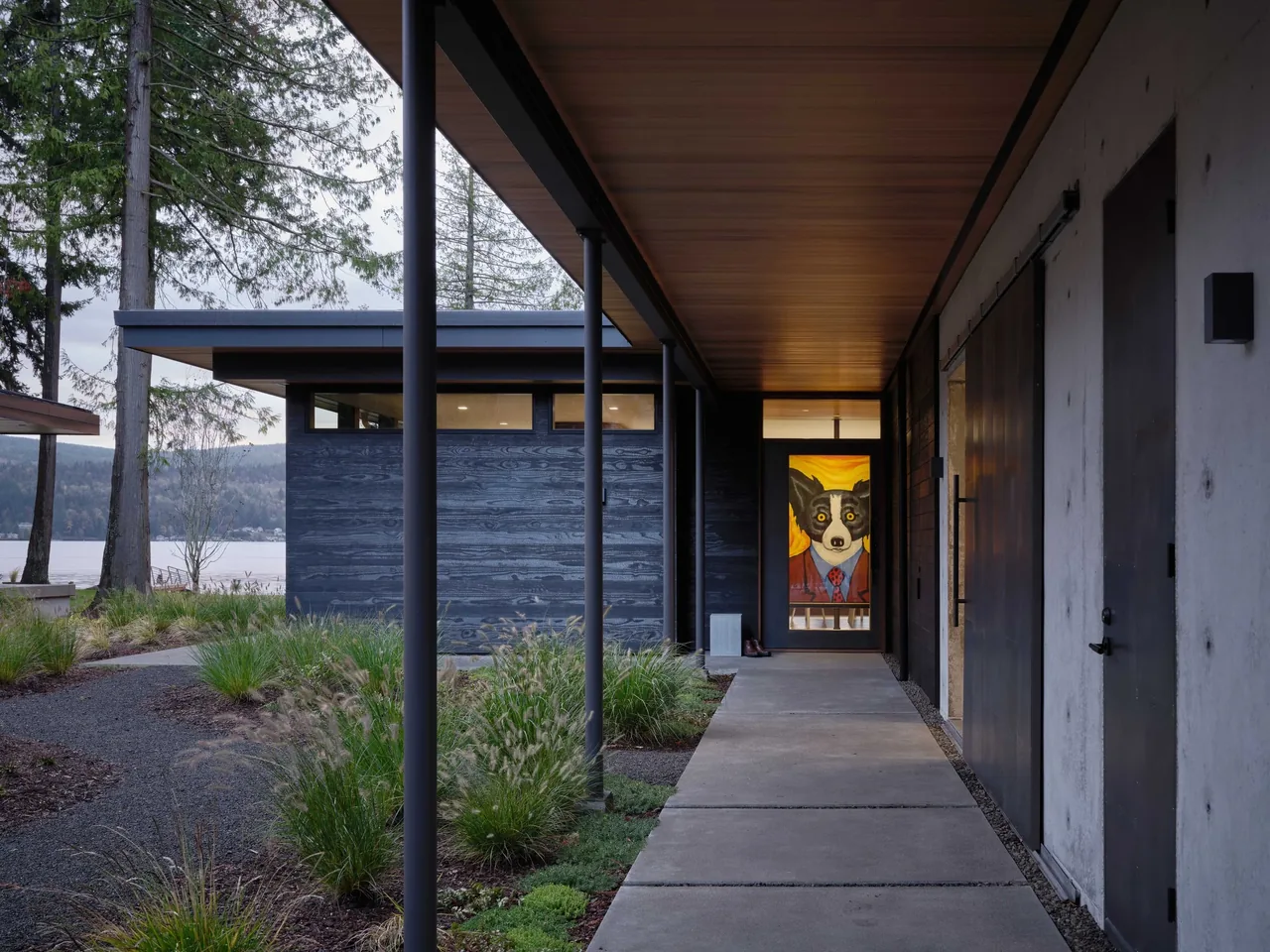 Covered exterior walkway featuring dark wood siding and glass door with dog portrait at the entrance of Gamer HQ.