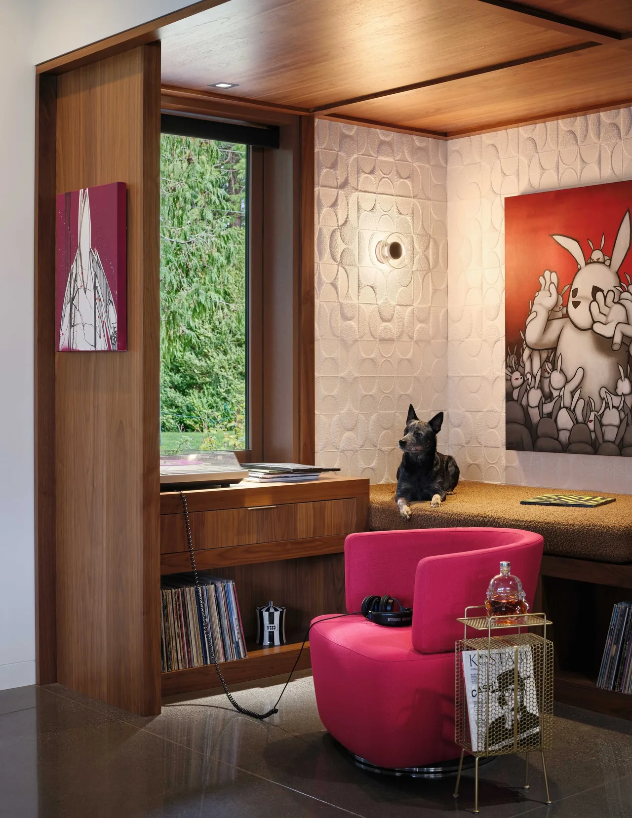 Modern reading nook features built-in bench, wood ceiling, and bright pink armchair with headphones and records.