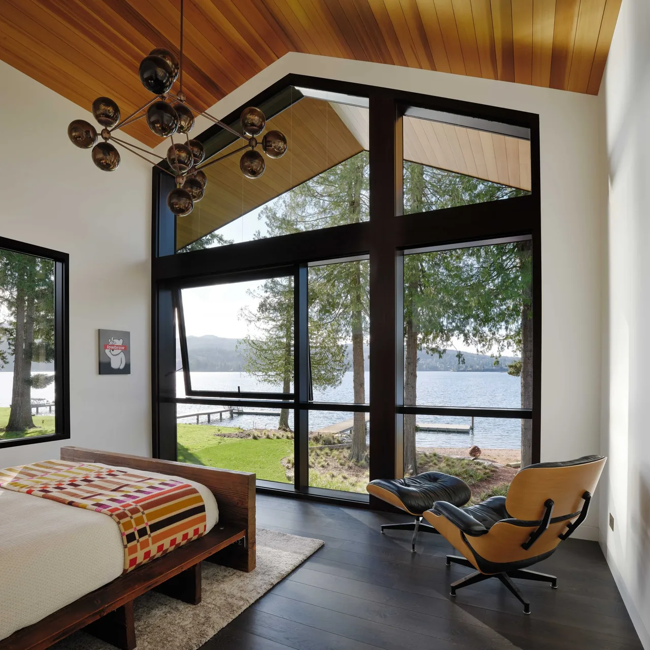 Bedroom with expansive corner windows and a wooden ceiling looking out over a lake at Gamer HQ.