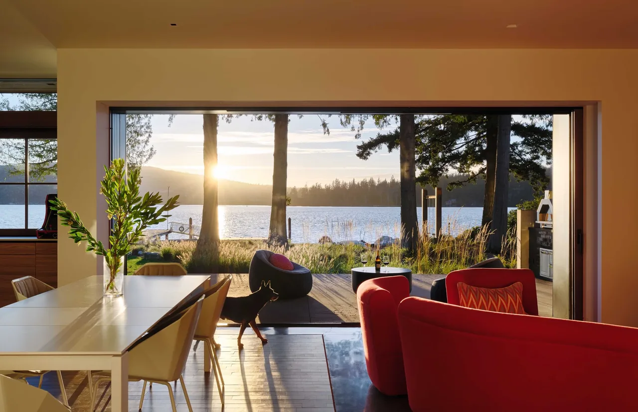 The Gamer HQ project features an open dining and living space with expansive lake views through a full-width sliding glass door.