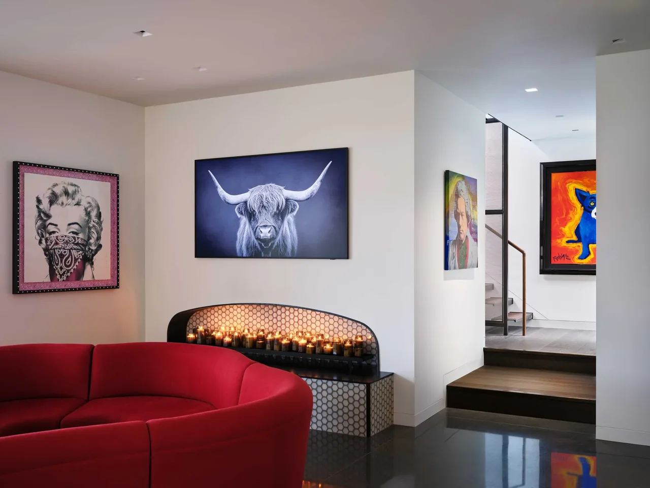 Living area featuring a curved red sofa, portrait artwork, and a recessed candle wall in a modern setting with stairs visible.