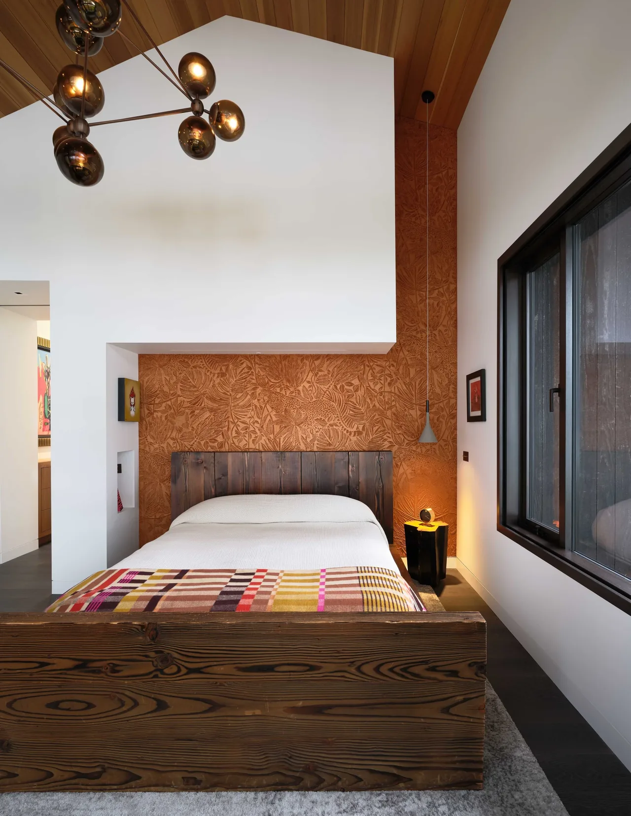 Bedroom with vaulted ceiling and a textured rust-colored accent wall behind a wooden bedframe.