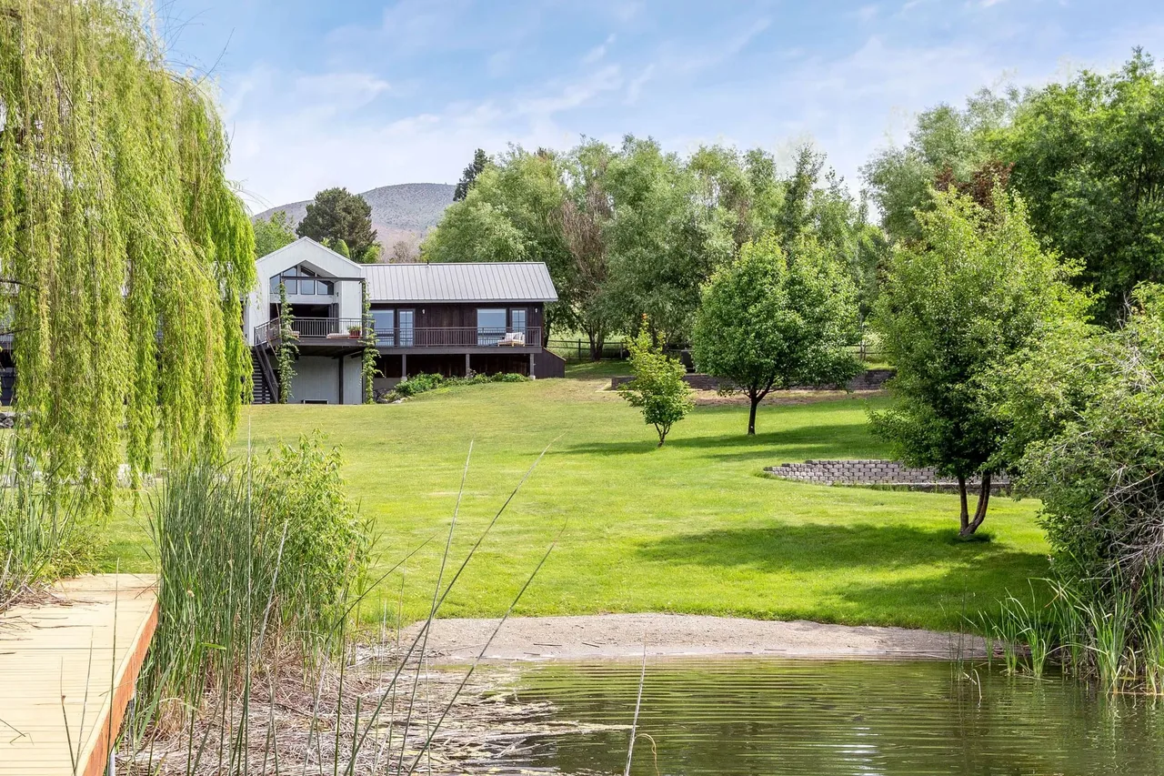 The Roses Lake Residence features a metal roof and dark siding with a spacious lawn to a lakeside dock.