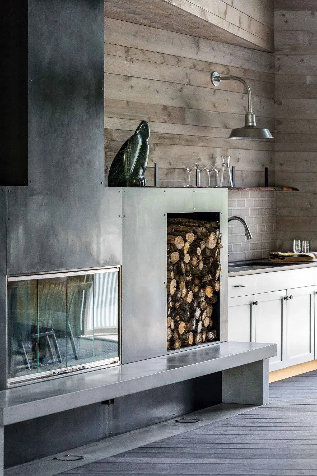 The Roses Lake Residence features a metal fireplace with integrated wood storage in an open kitchen space with white cabinetry.