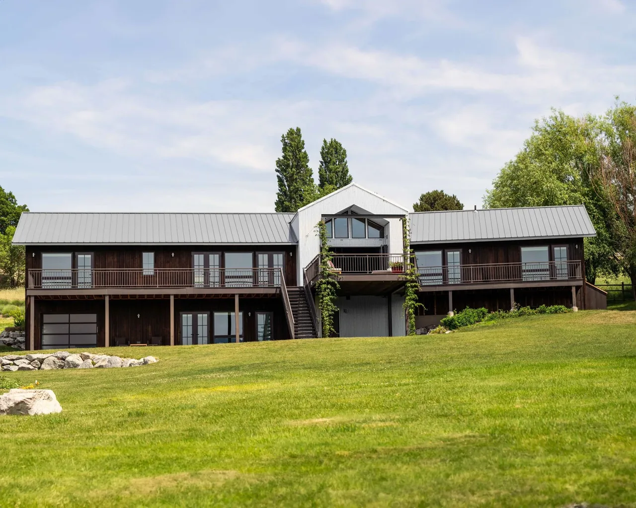 The Roses Lake Residence features dark wood siding with a light gray metal roof and a landscaped green lawn.