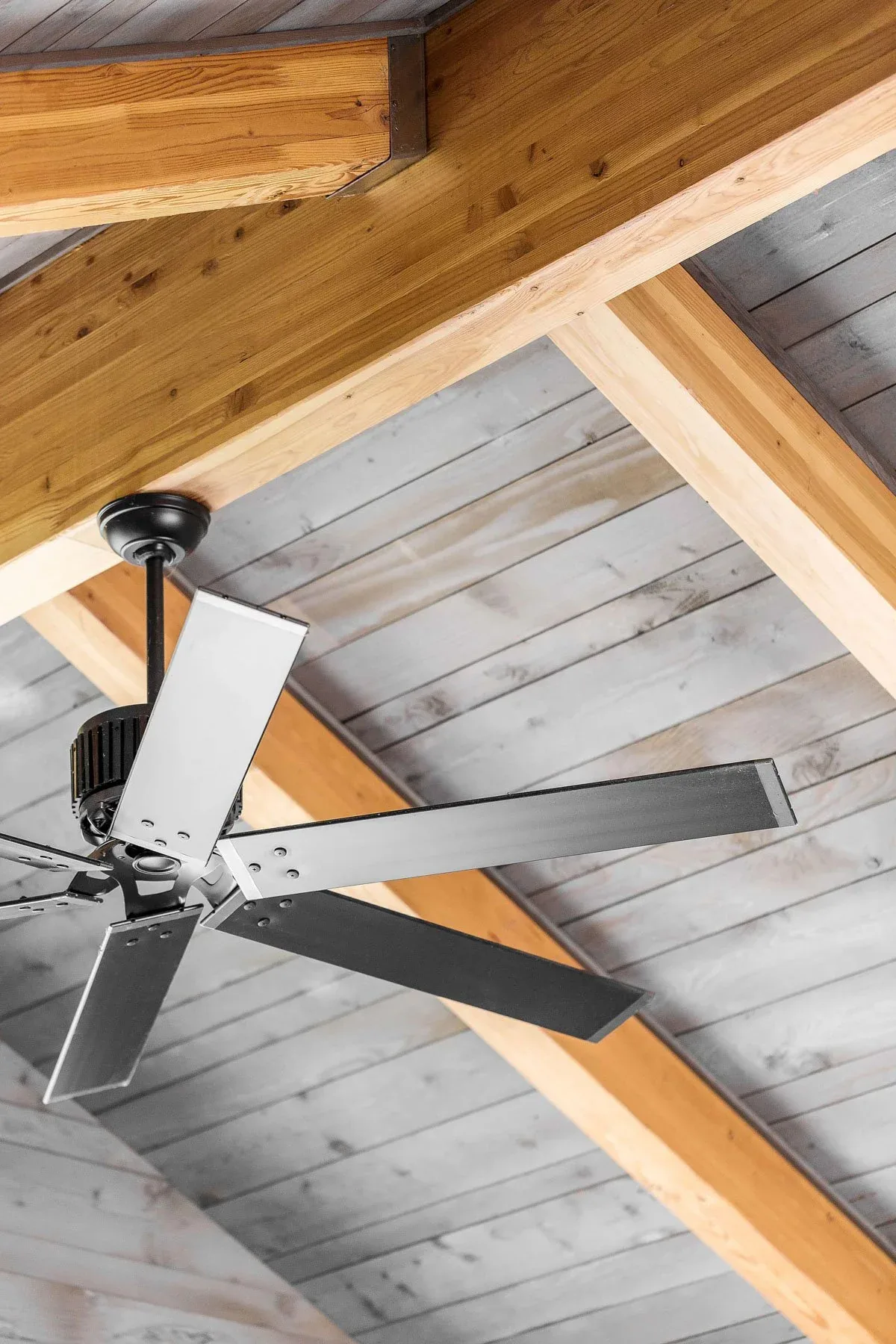Metal ceiling fan installed on a vaulted ceiling featuring exposed wood beams and wood planks.