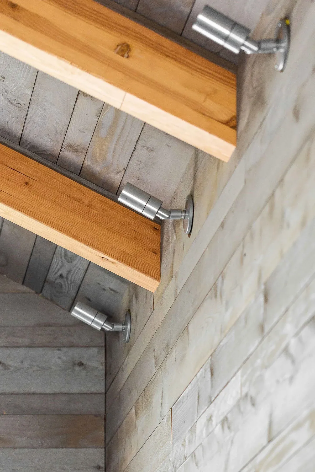 Rustic wood shelves fixed with metal brackets on a textured gray wood plank wall.