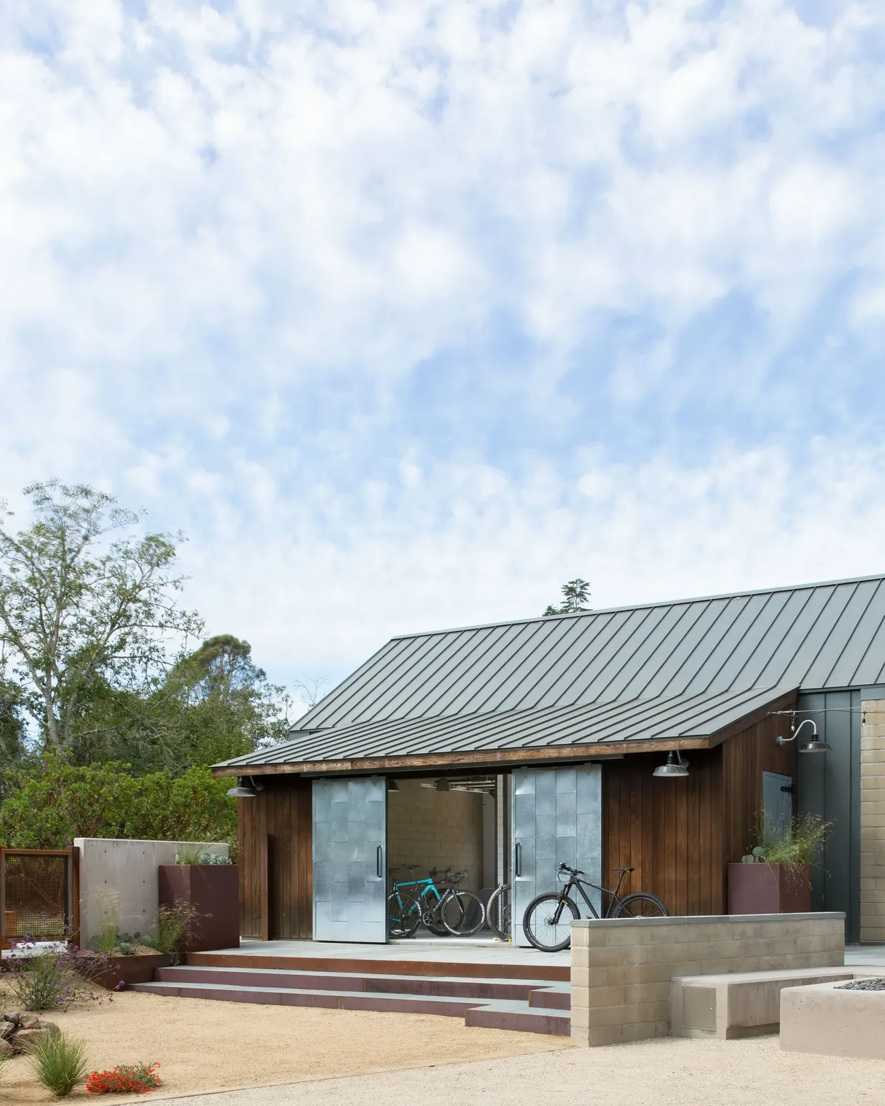 Small wood-paneled building with metal roof and metal sliding doors, showing bicycles inside an open garage area.