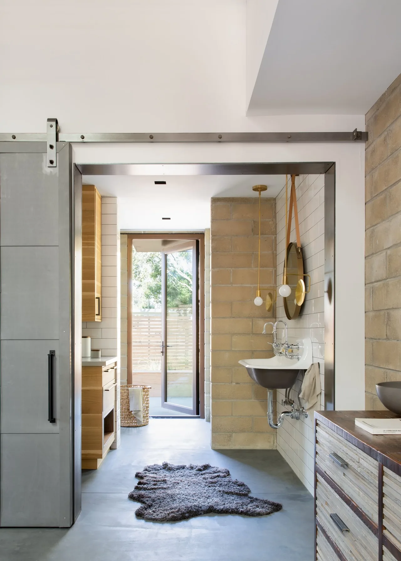 Hallway view featuring a wall-mounted sink, brass pendant lights, and textured brick walls with a glass door at the end