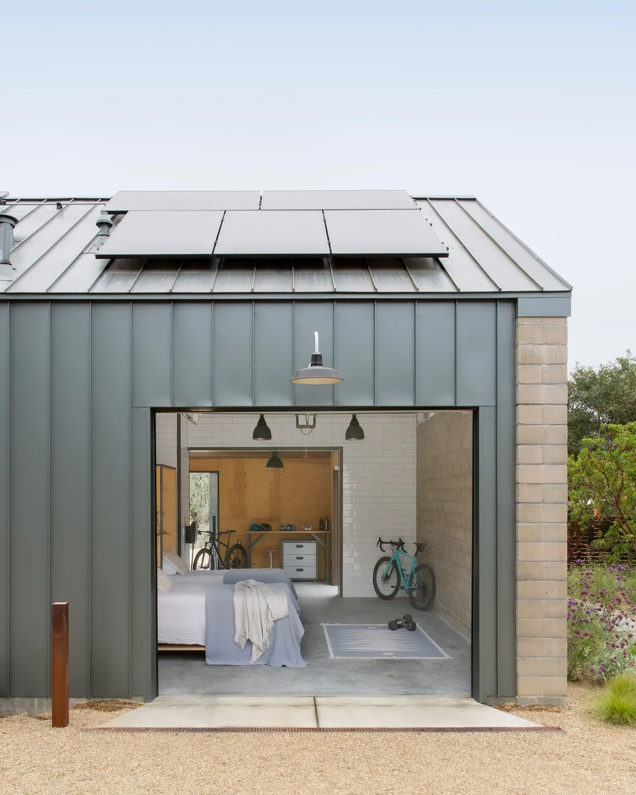 The Sonoma Farmhaus features a modern garage-style bedroom opening to the outdoors with metal siding and solar panels on the roof.
