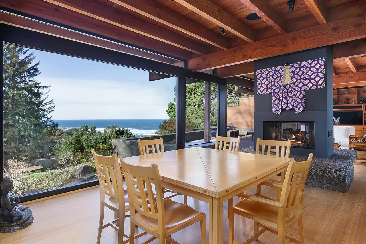 Dining space featuring wood ceiling beams, a stone fireplace, and expansive floor-to-ceiling glazing with ocean views.
