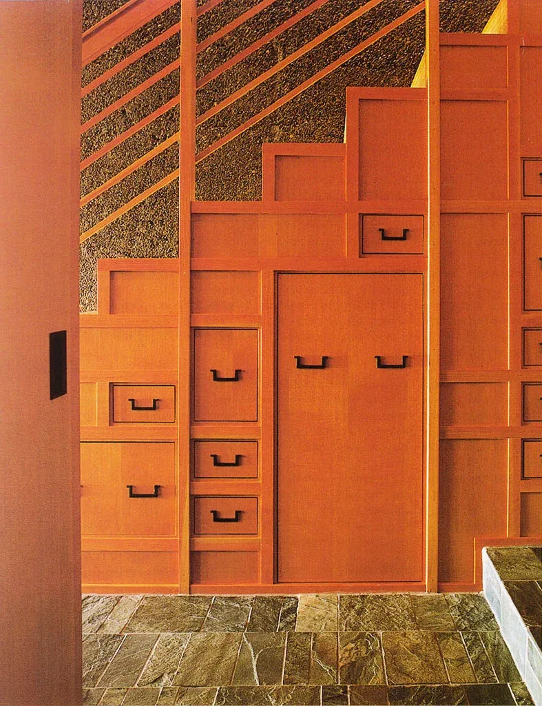 Wood-paneled built-in storage with multiple drawers and cabinet doors, set against a textured wall and stone tile floor.