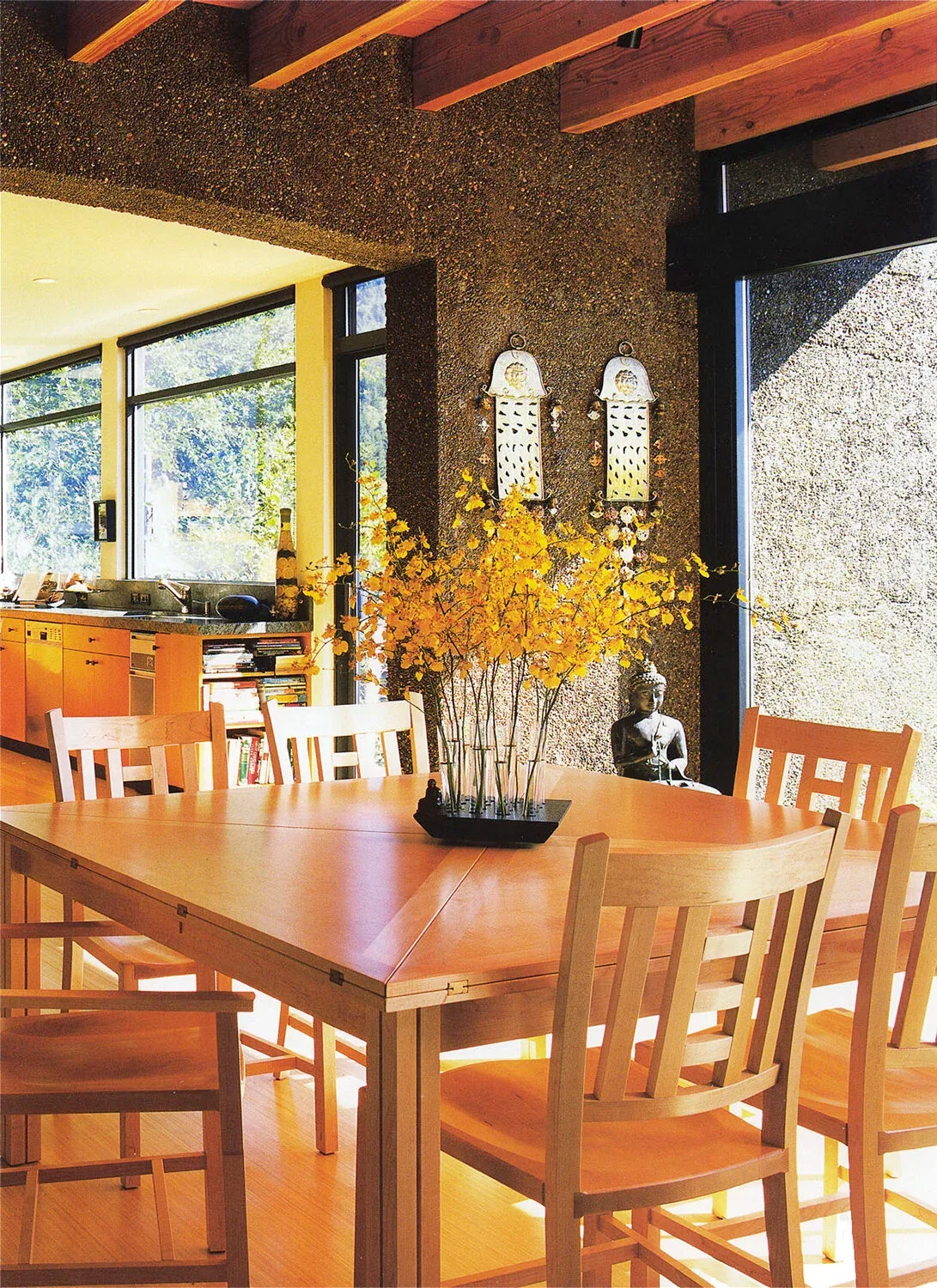 Dining room with wooden furniture and large windows features a textured accent wall and decorative elements including a Buddha statue.