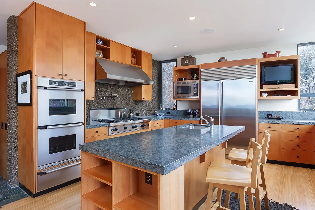 Kitchen in Horizon Hill House features a spacious island with stone counters and wood cabinets alongside stainless steel appliances.